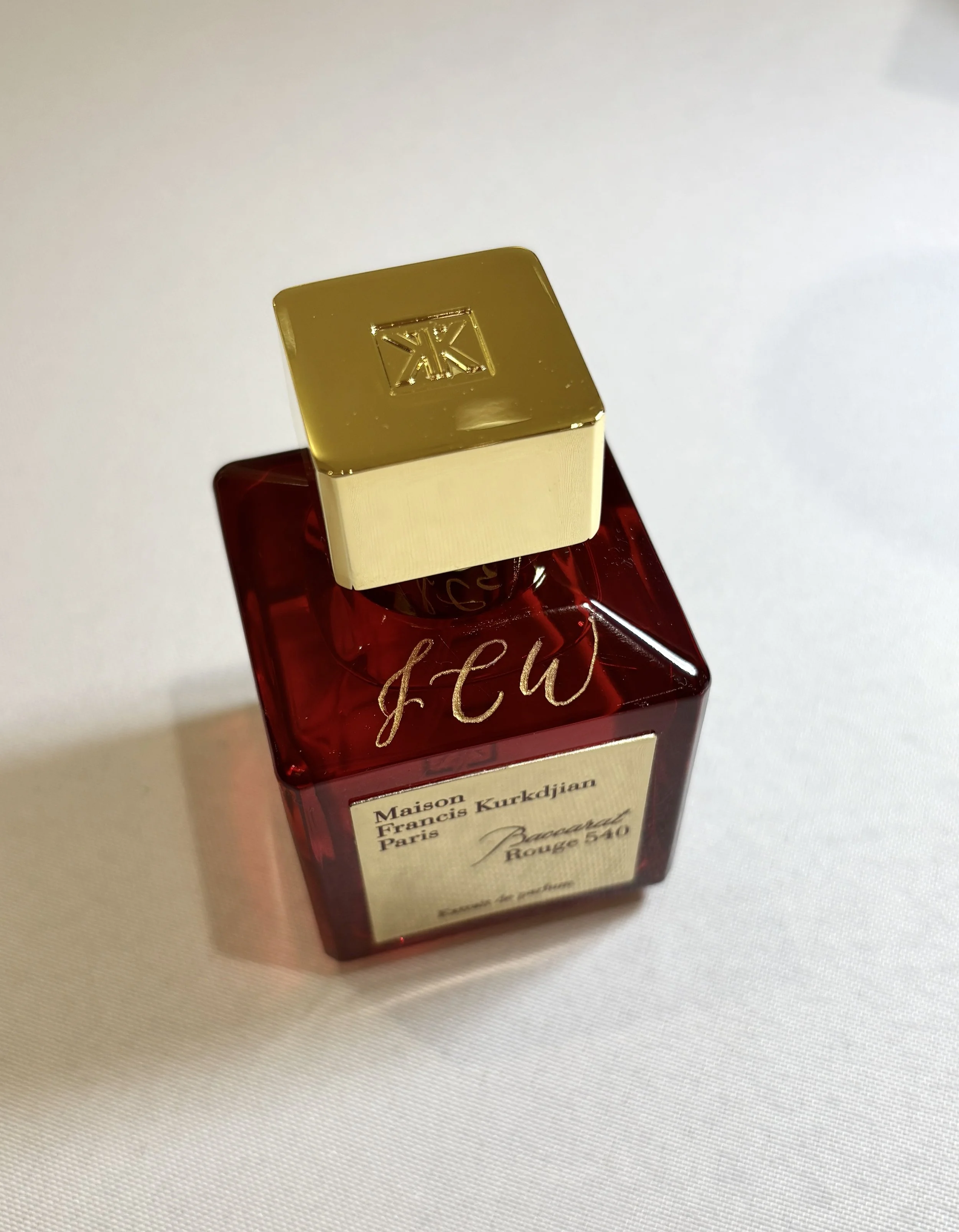 Live engraving in Denver, CO on Red perfume bottle with a gold cap on a white surface.