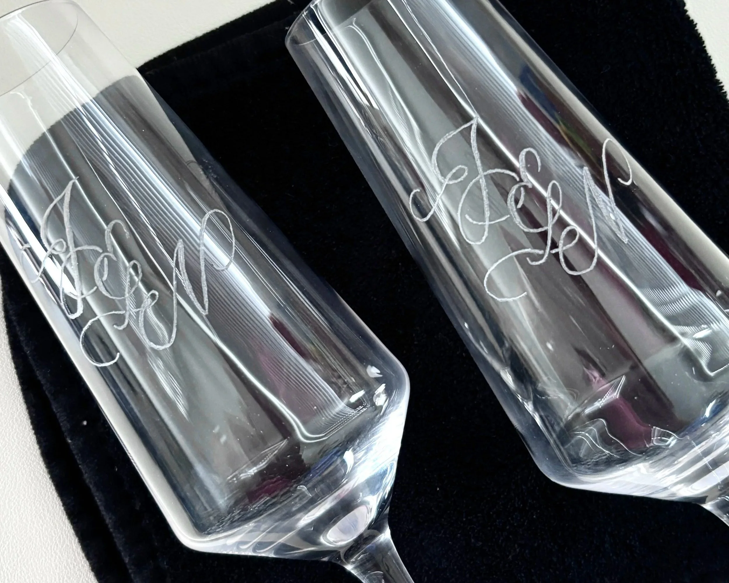 Two champagne flutes have been engraved in a flourished design with the letters "J&N" for a wedding gift.
