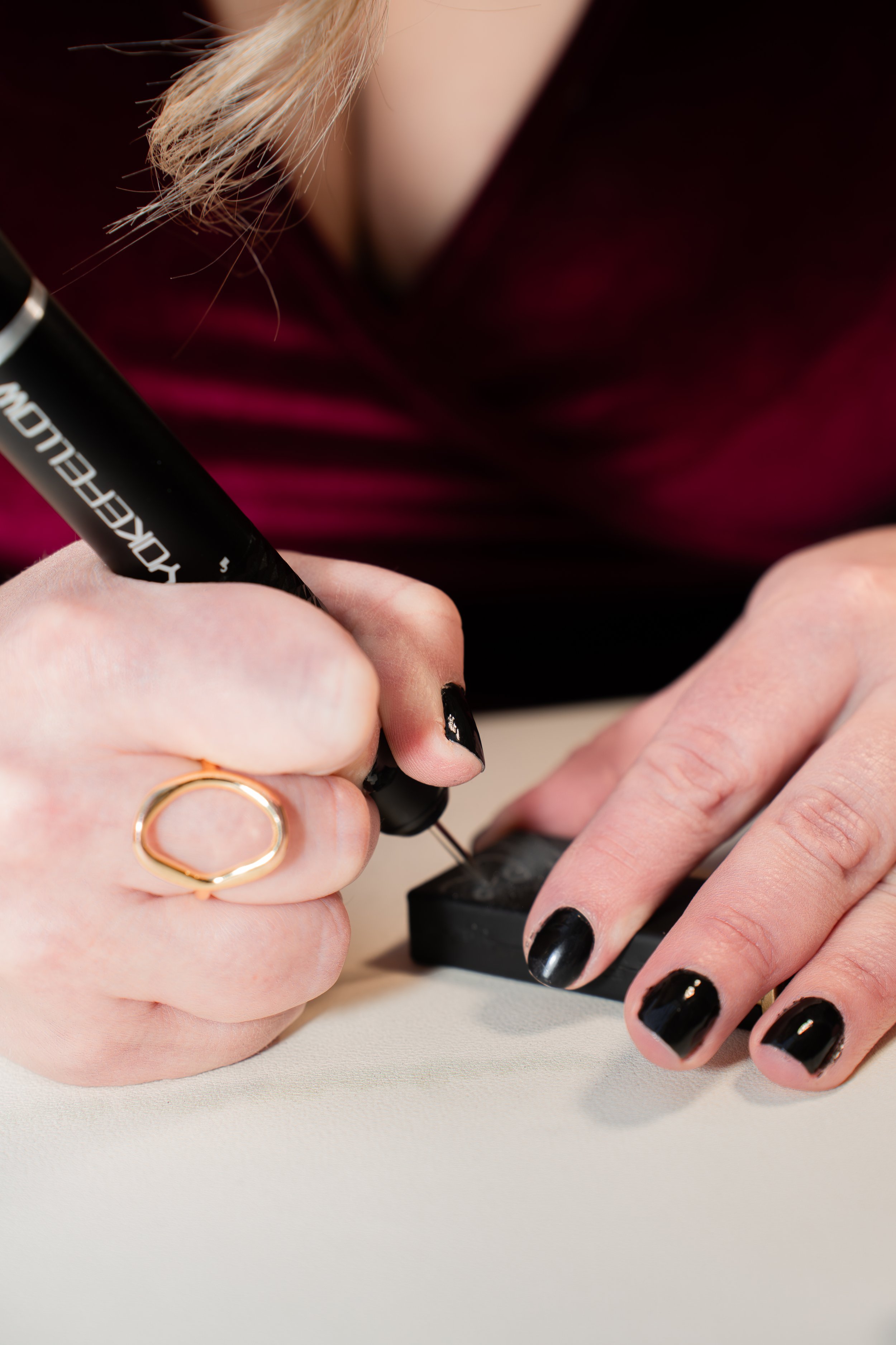 Person with black nail polish engraving a lighter by hand, wearing a gold ring.