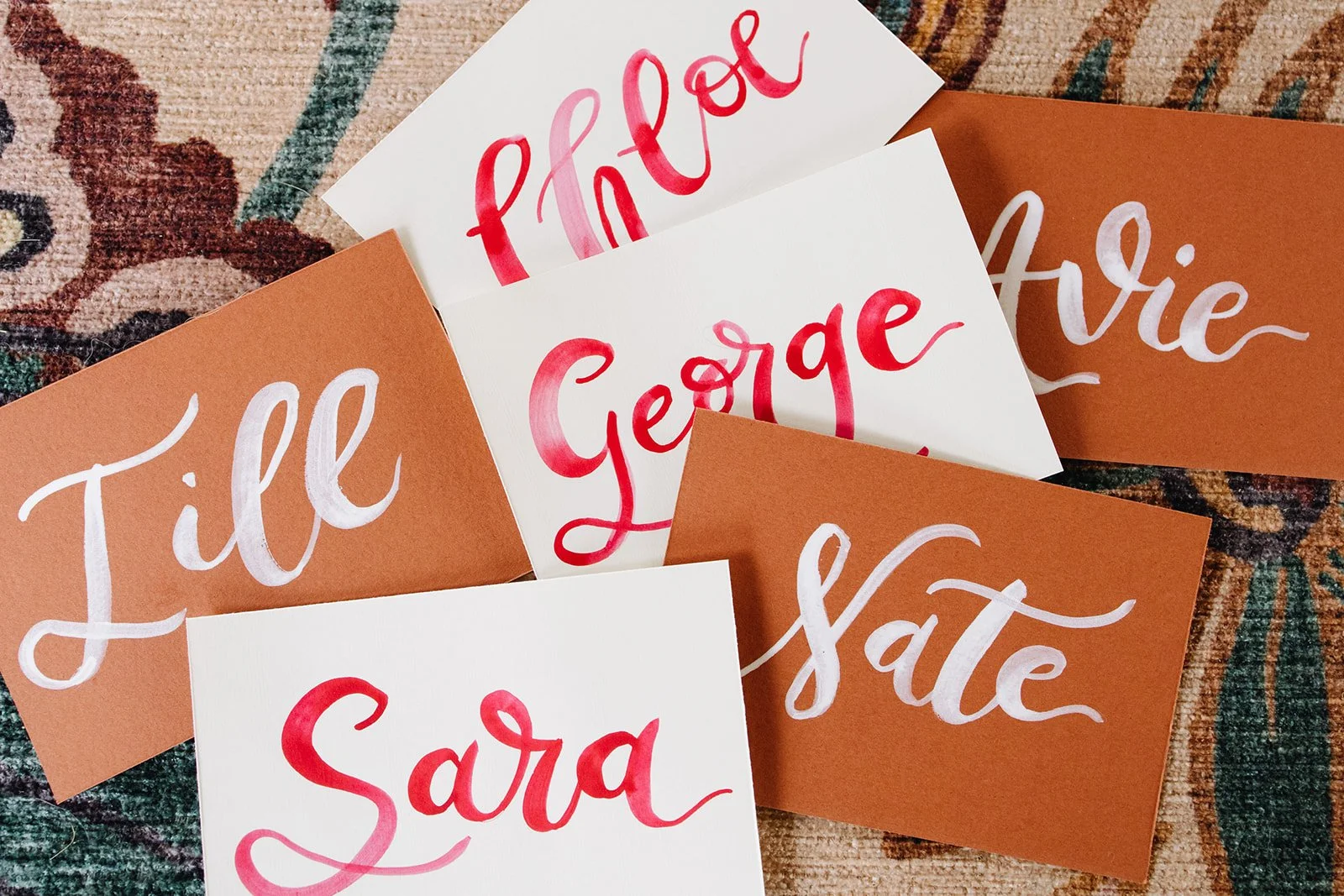 Several pieces of paper with handwritten names and words, including 'Sara,' 'Gorge,' 'Jille,' and 'Aust' on a patterned carpet.