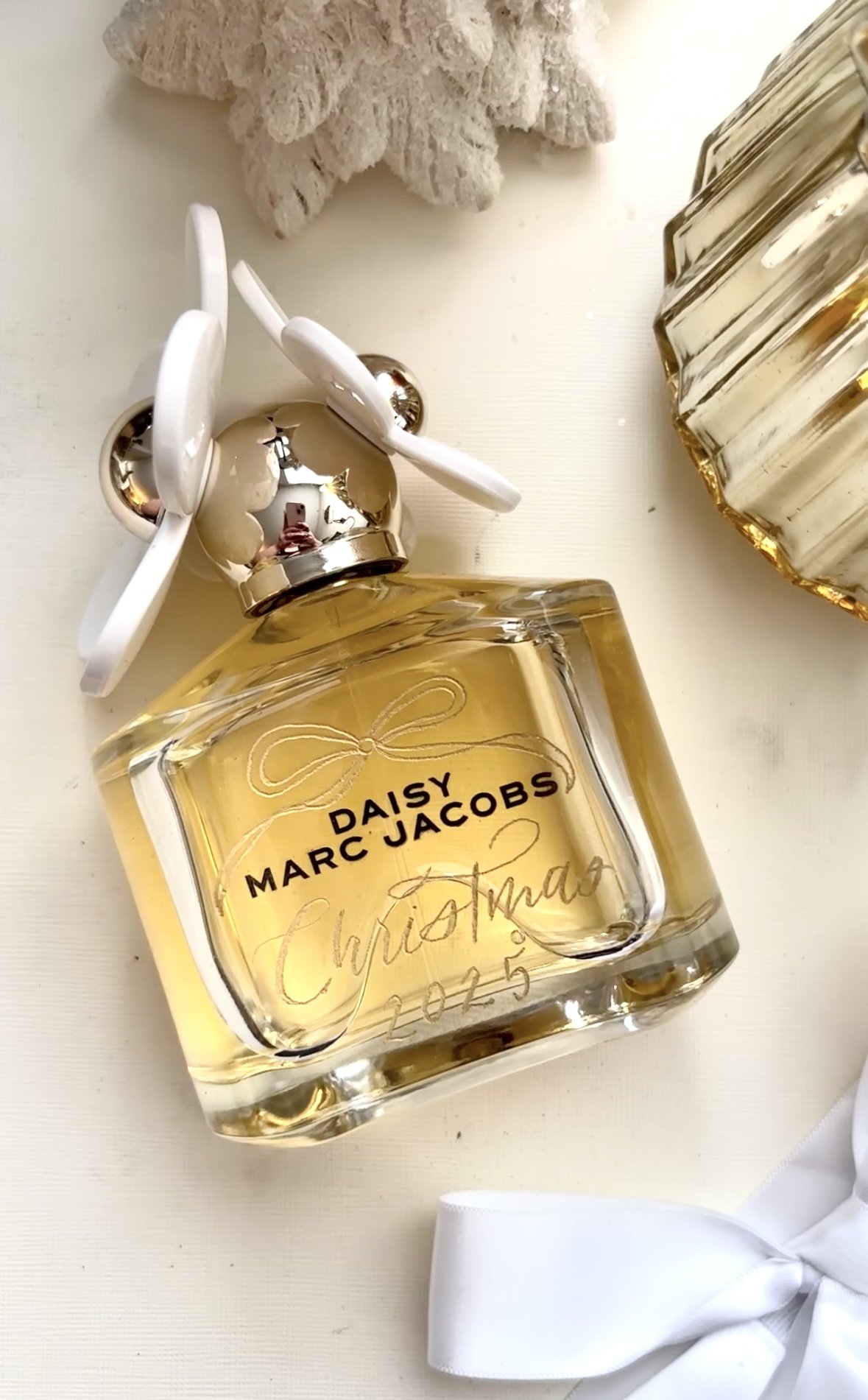 Daisy Marc Jacobs perfume bottle engraved in-studio in Denver, CO with 'Christmas 2025' with a white Christmas tree and decorative items nearby.