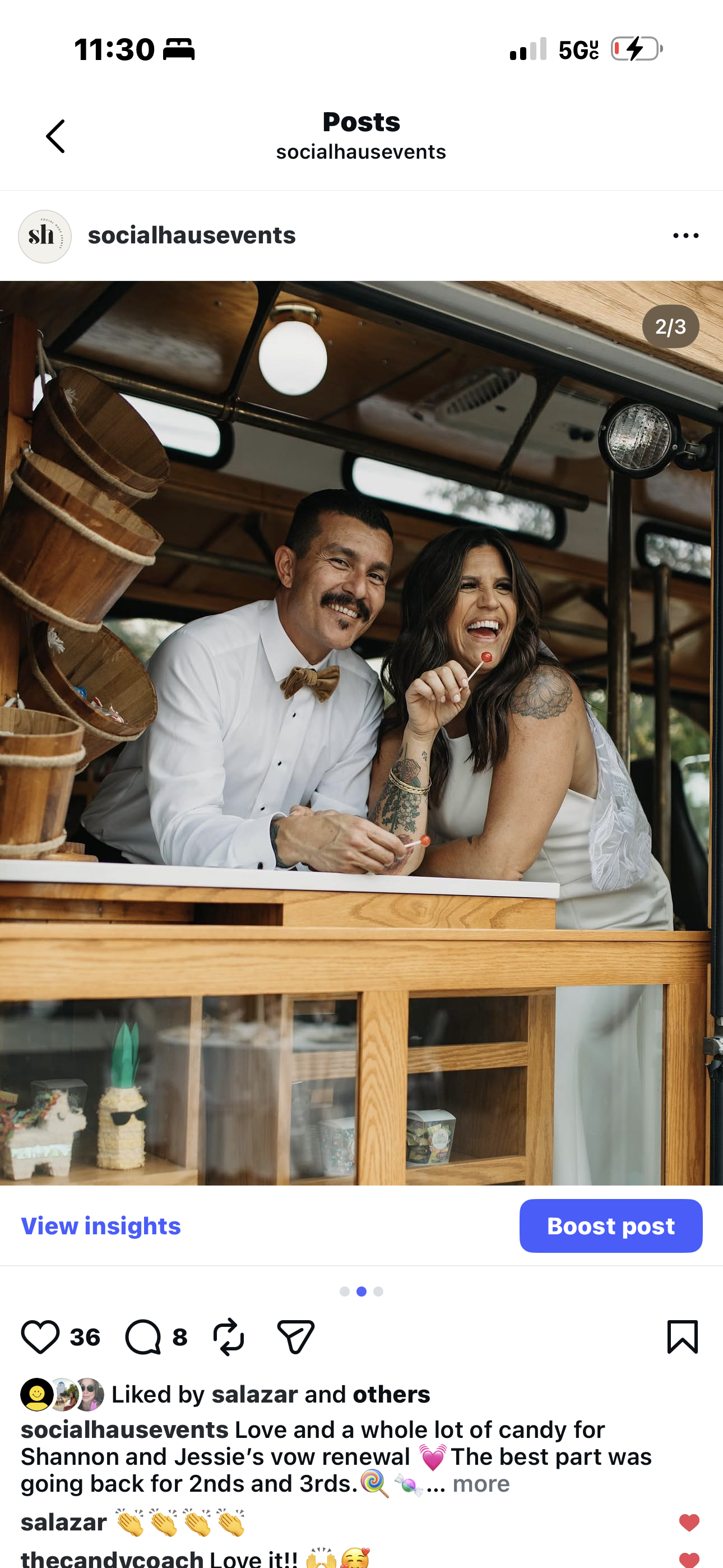 A man and woman at a celebration, smiling and holding lollipops, with a display case of cakes and treats in the foreground.