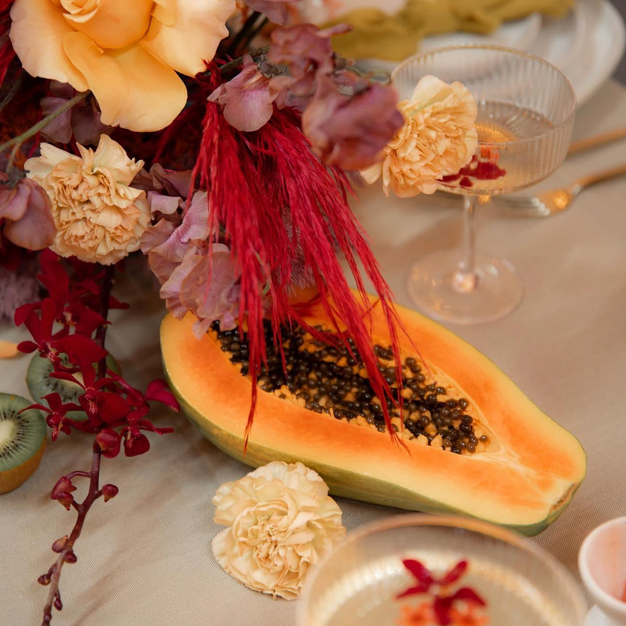 Half of a papaya on a dining table surrounded by flowers and desserts