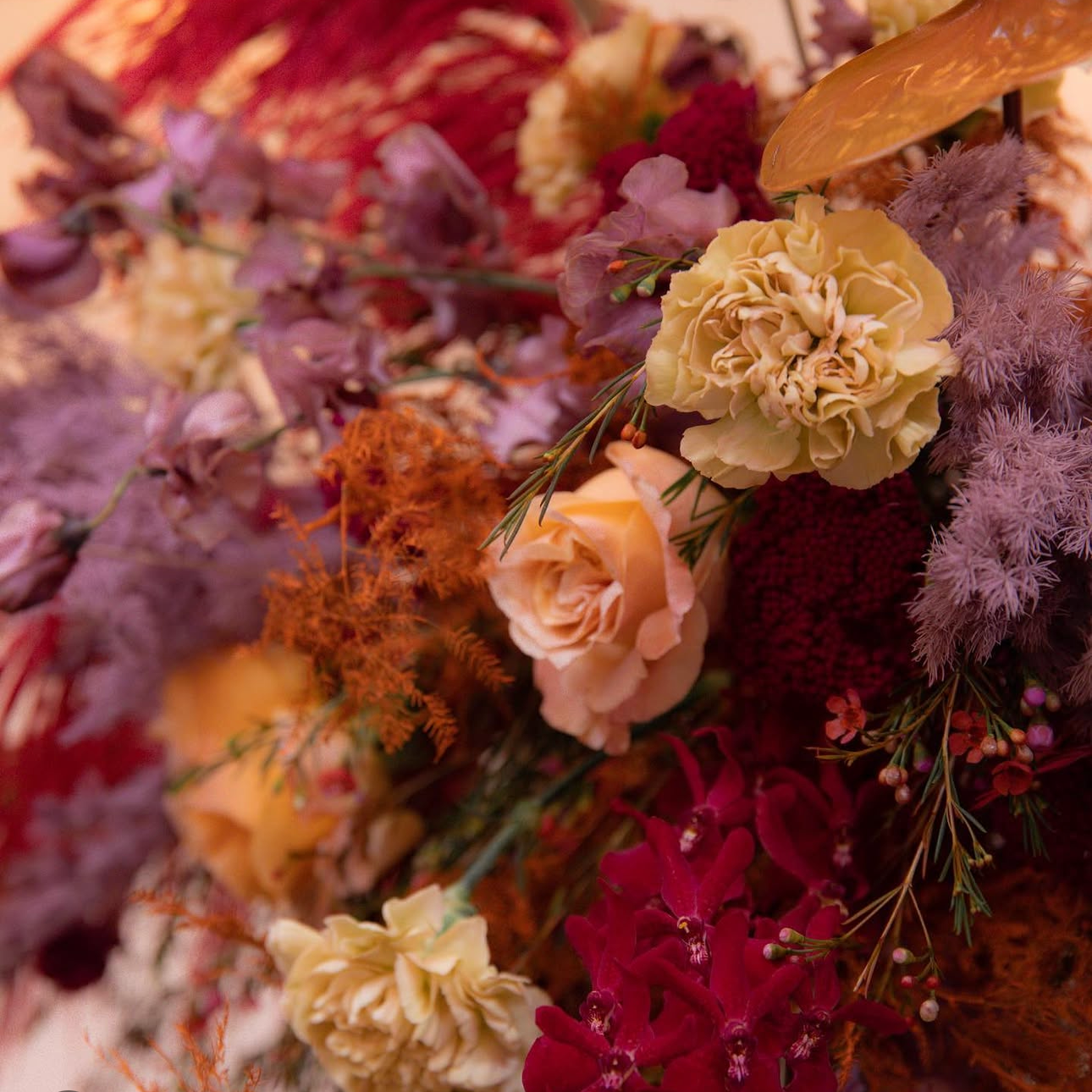 Close-up of a colorful assortment of flowers including cream roses, purple and red blooms, and orange and pink accents.