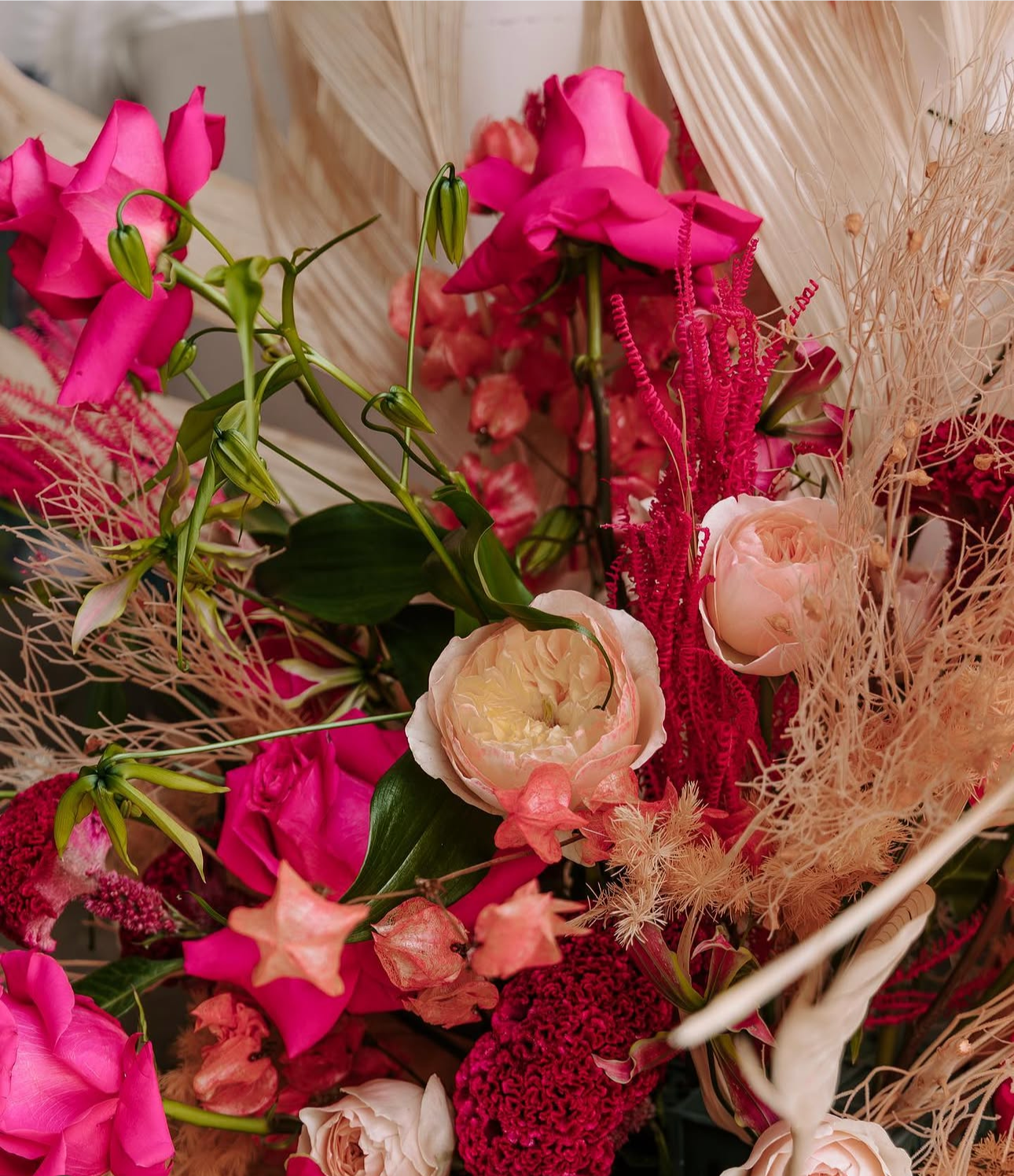 A colorful flower arrangement featuring pink, peach, and cream flowers with dried beige foliage.