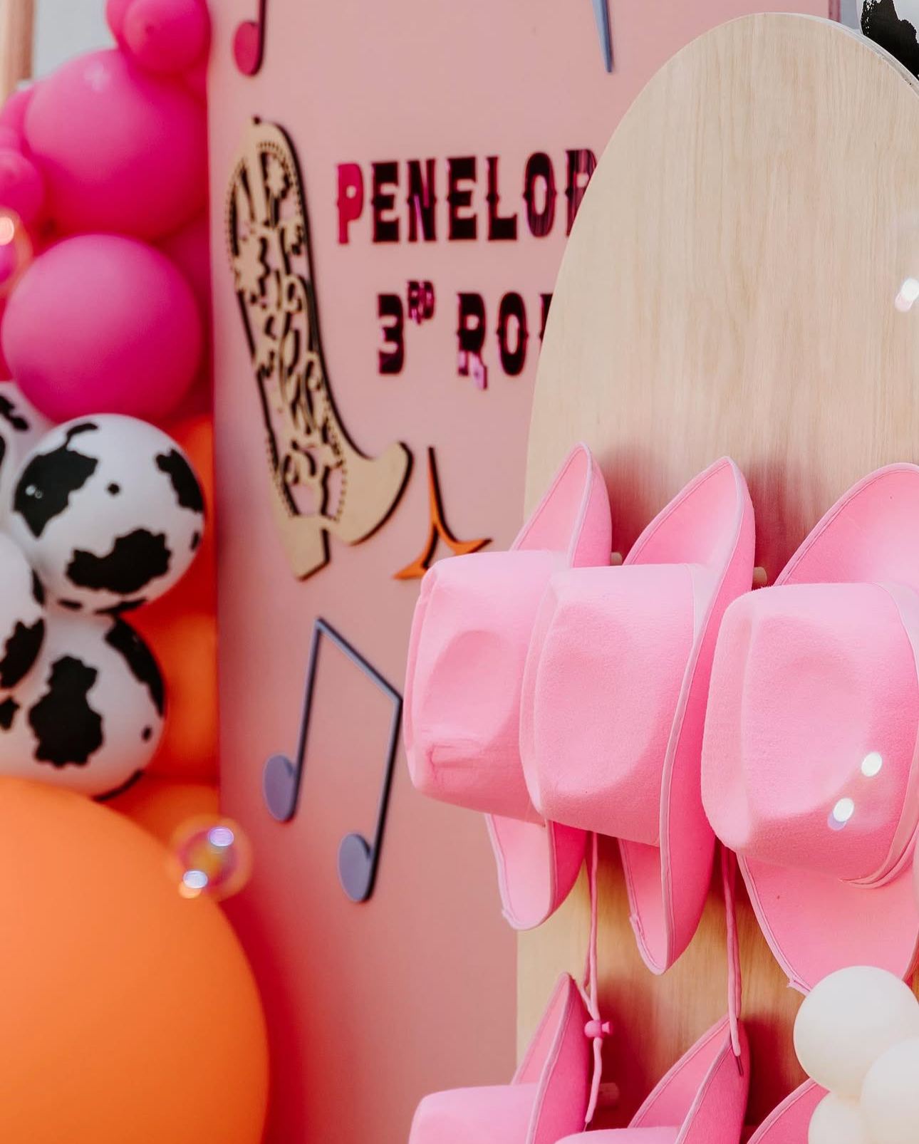 Pink decorative shoe for Pinelope 3rd birthday with pink balloons, a paper cow print, and musical note shapes on a pink background.