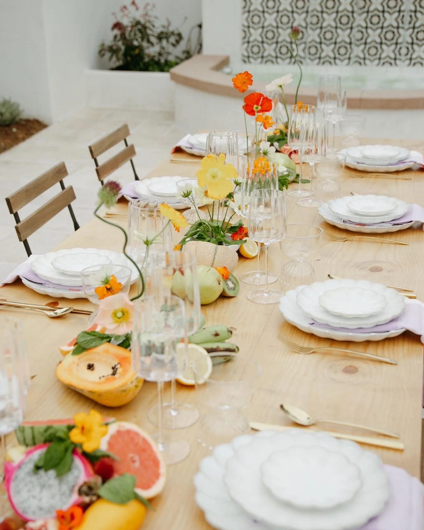 A table set for a meal with white plates, clear glassware, and colorful flower centerpieces on a wooden table.