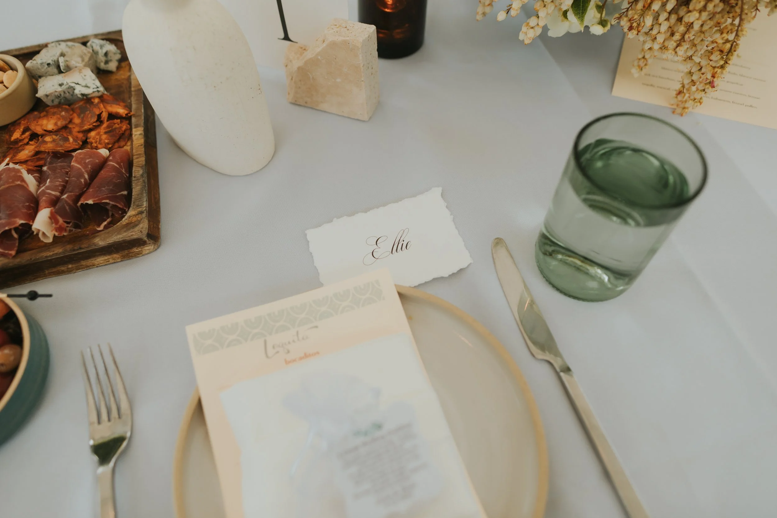 Table setup with decorative items, a glass of water, and a place card with the name 'Elie' at a formal event.