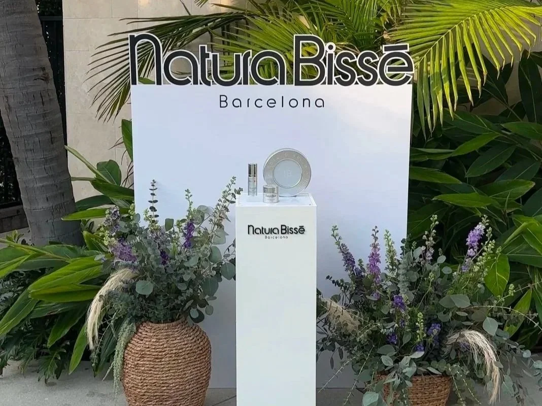 Display stand with skincare products from Natura Bissé, Barcelona, set against a backdrop of green plants and flowers in baskets.