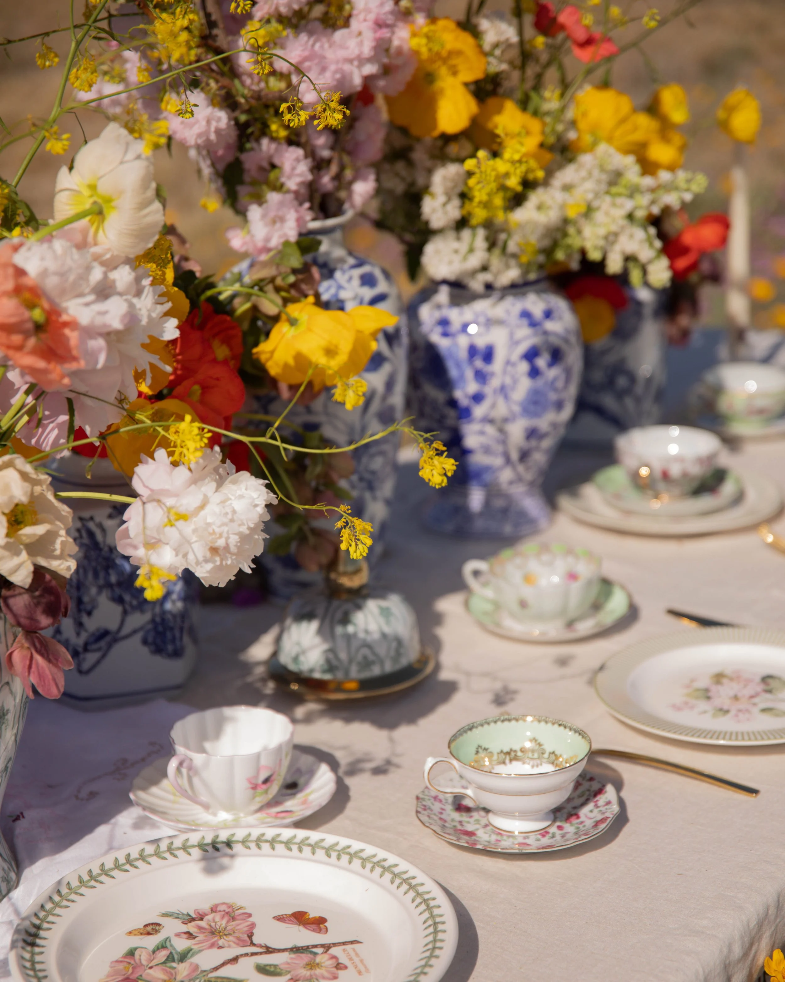 A close-up view of a display of vintage teacups, saucers, and porcelain vases filled with colorful fresh flowers on a table.