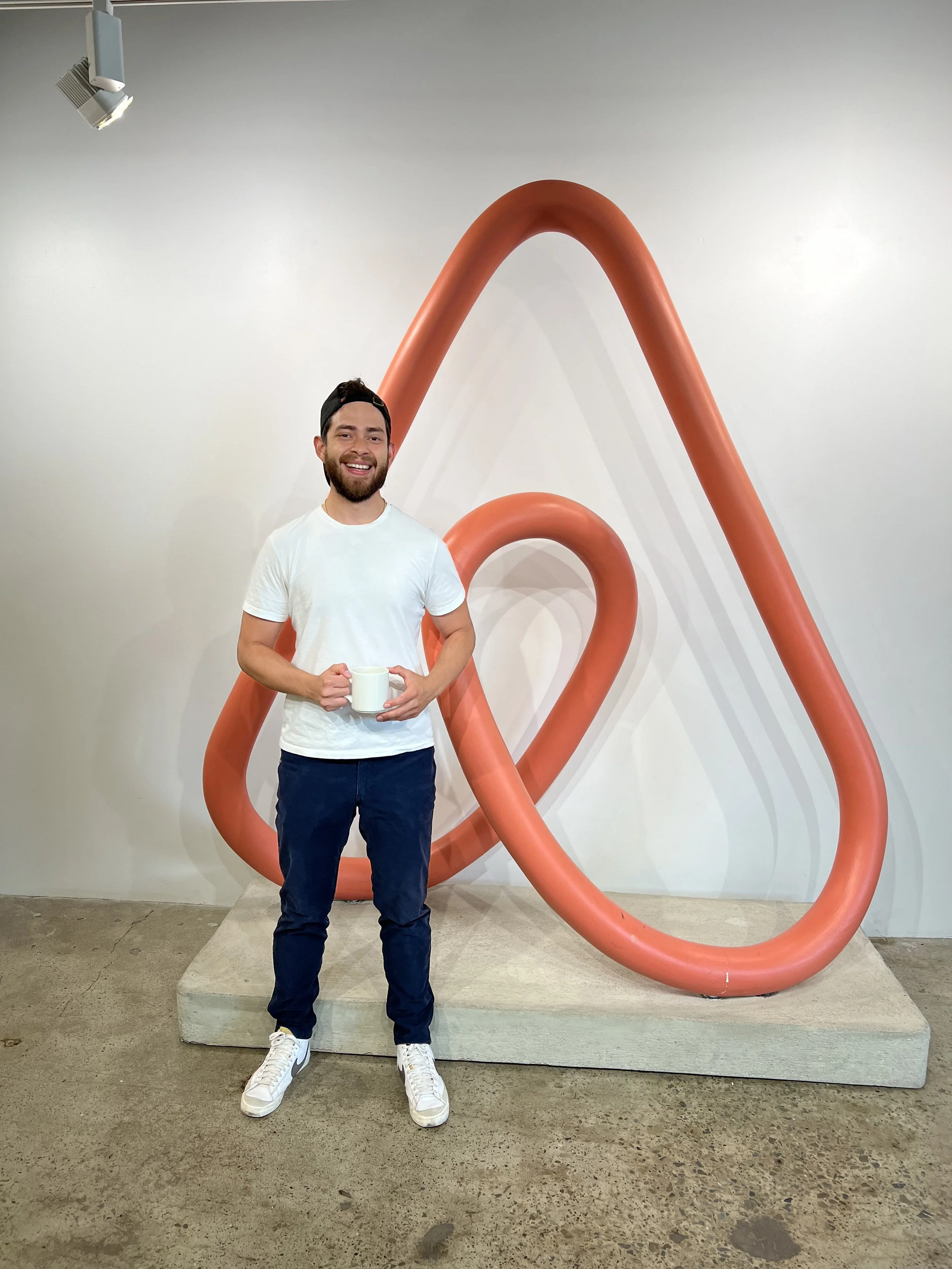 Manuel, the author, standing in front of the airbnb logo statue holding a cup of coffee!
