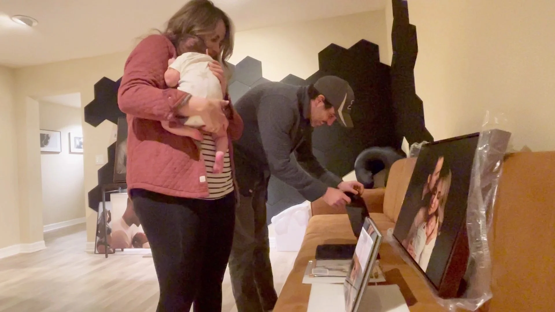 A woman wearing white archival gloves carefully lifts a matted photo print from a black presentation box, surrounded by several large canvas family portraits on a dining table.