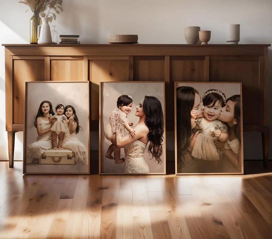 Three large, custom-framed fine art portraits of a mother and her daughters are leaned against a wooden sideboard in a sunlit home.