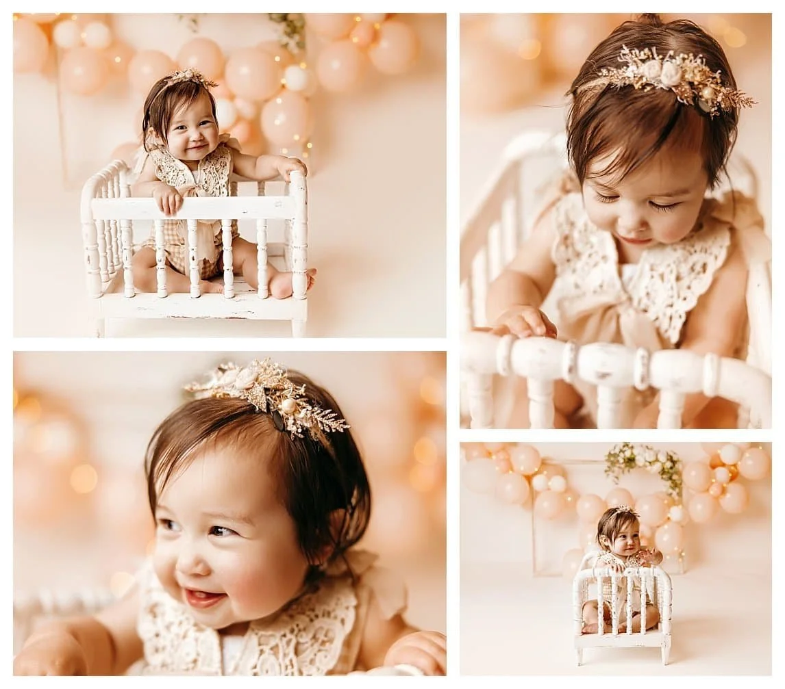 A first birthday milestone collage of a baby girl in a lace romper and floral headband. She sits in a white vintage crib prop against a cream backdrop with a peach balloon arch and fairy lights.