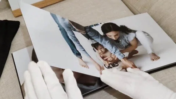 Hands in white archival gloves open a custom lay-flat heirloom photo album showcasing a Portland family portrait session. This premium print product is perfect for families wanting physical, heirloom photography pieces.
