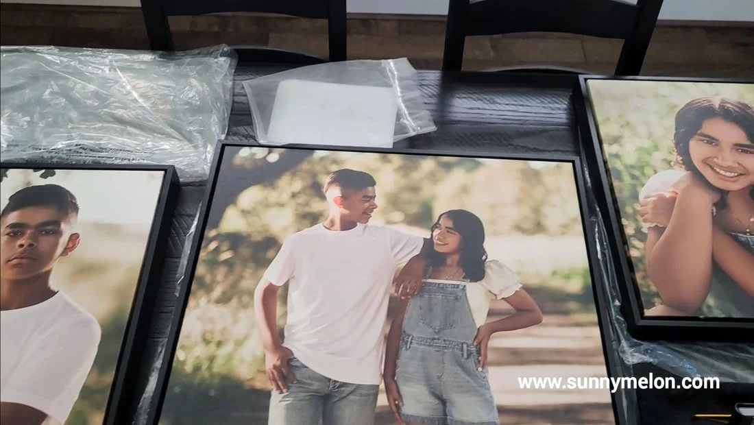 High-end black-framed canvas portrait prints from a sibling lifestyle session displayed on a dark wood table in a Portland, Oregon studio.