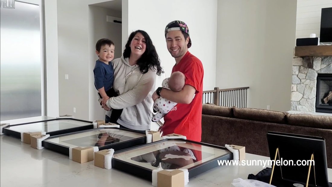Behind-the-scenes family photo capturing parents, a toddler, and a newborn revealing custom large-format framed wall art prints delivered to their Hillsboro, Oregon home.