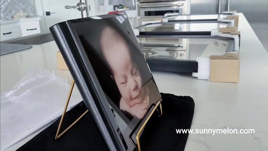 Premium leather photo album with a glossy acrylic newborn portrait cover displayed next to large-format matted wall art frames in West Linn, Oregon.