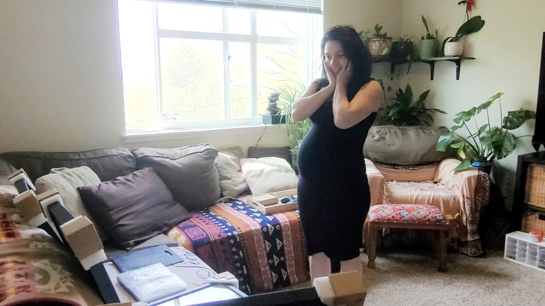 Candid lifestyle portrait of a happy pregnant client reacting with joy during a personalized fine-art print reveal session at home.