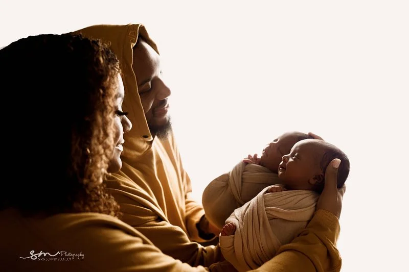 Tender backlit portrait of Damian Lillard and Kay'La Lillard smiling down at their newborn boy/girl twins, who are swaddled and being held close during their Portland, Oregon photo session.