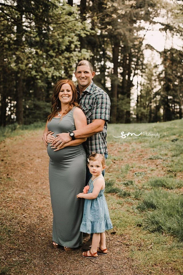 A high-end studio maternity portrait of a pregnant woman with blonde hair and a leg tattoo, reclining on a sofa draped in layers of sheer peach tulle fabric.