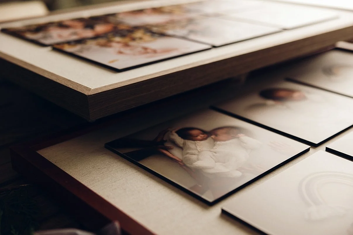 Close-up of high-quality framed newborn photography prints and wall art products featuring a baby in a white knit outfit, displaying professional studio finishes.