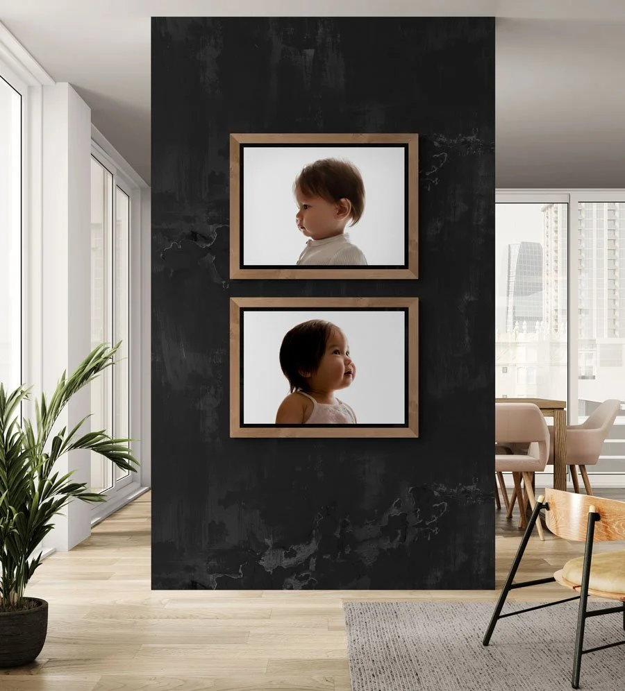 Two large, vertically stacked wooden frames featuring minimalist profile portraits of children, displayed on a textured dark grey accent wall in a modern, sunlit home.