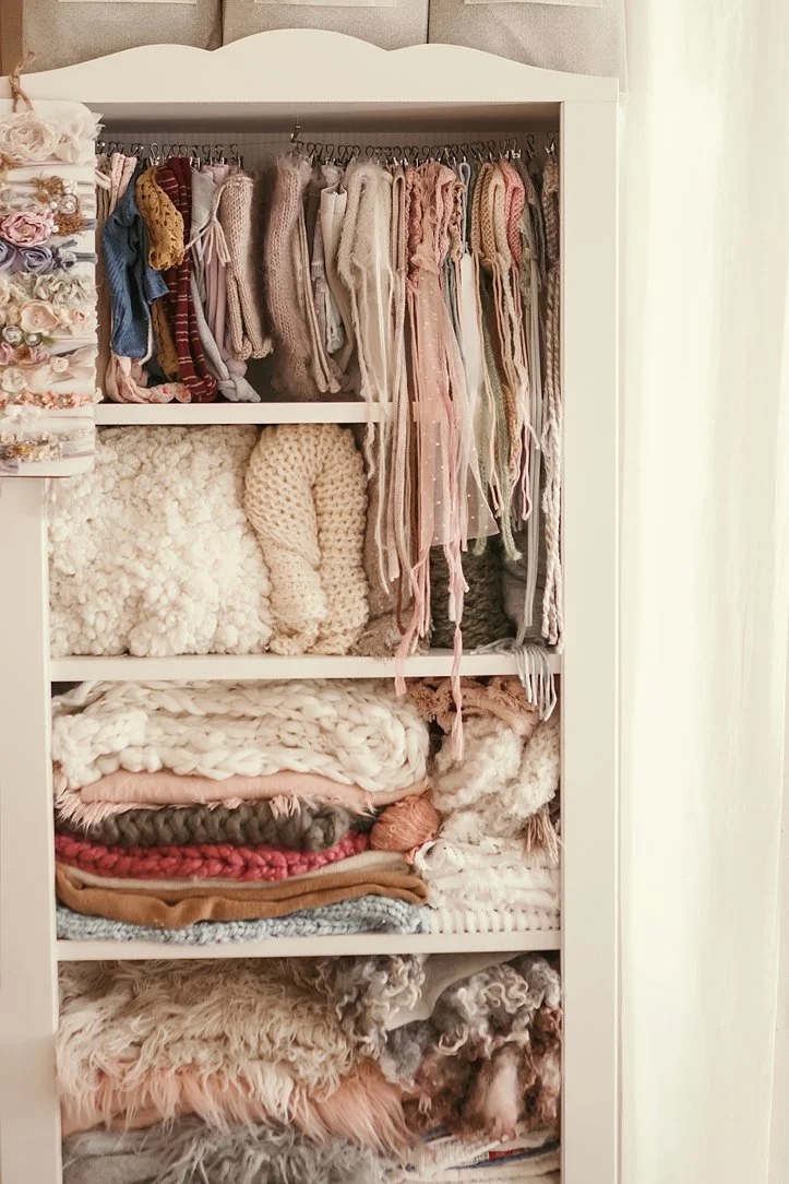 This behind-the-scenes look features a curated studio wardrobe and prop collection specifically designed for newborn and baby photography. The display includes a wide array of delicate floral headbands, hand-knit bonnets, and an assortment of high-qu