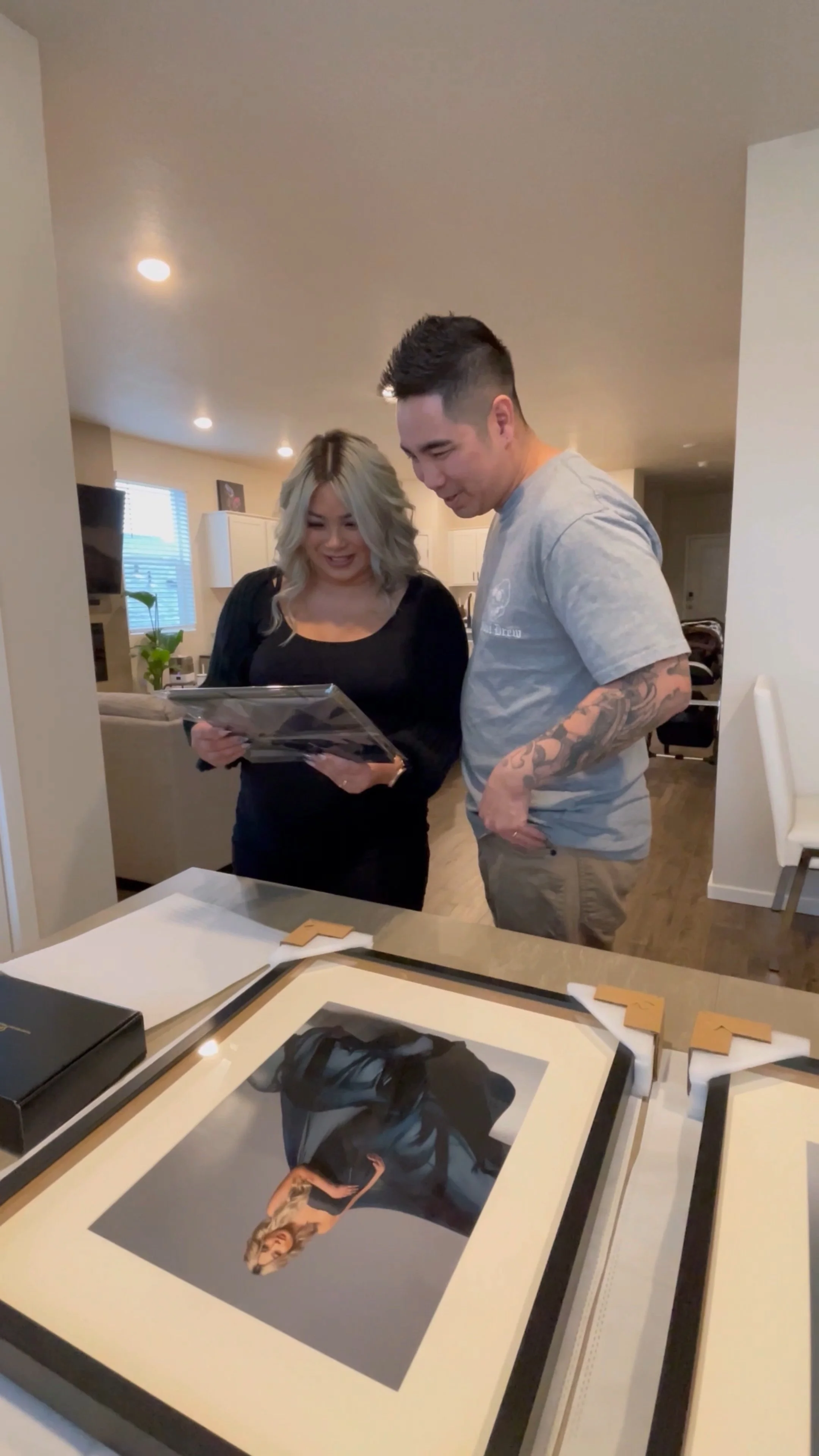 This image highlights the "reveal" stage of a high-end portrait experience, where clients see their finished milestones transformed into tangible art. The photograph captures a candid moment of discovery as a couple views a museum-quality framed and 