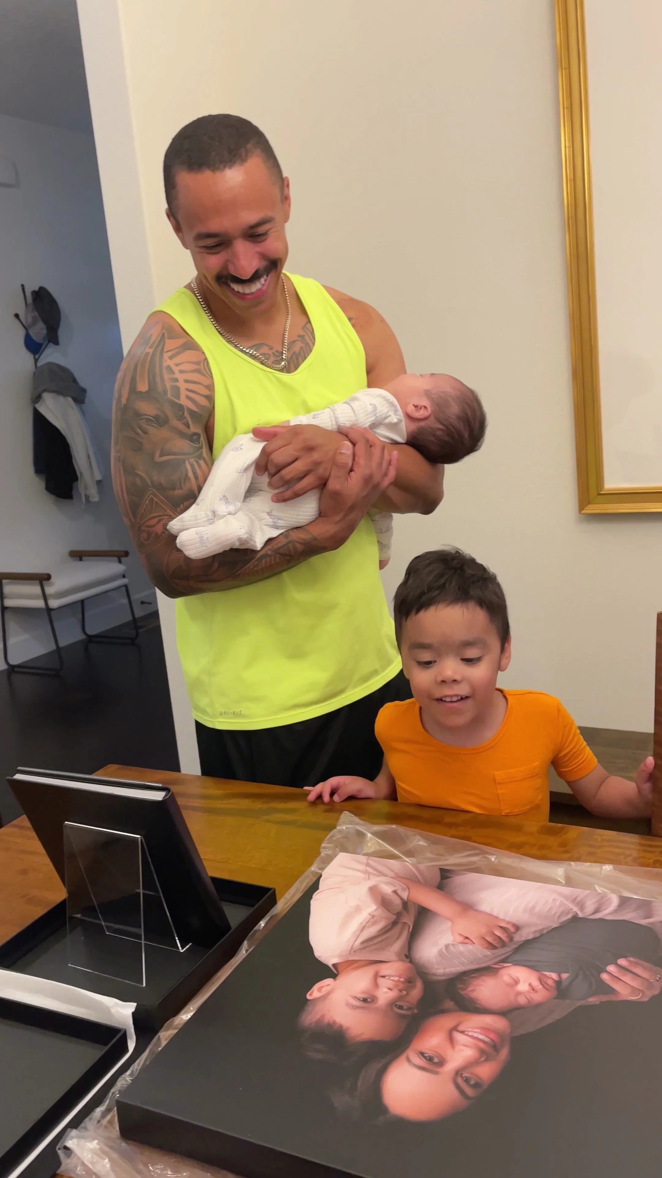 This image captures the heartfelt conclusion of a full-service portrait experience in the Portland metro area. The photograph shows a father and son unboxing their custom heirloom wall art and leather-bound album, highlighting the studio's dedication