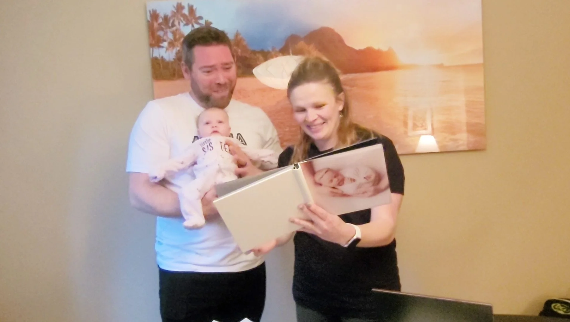 A lifestyle photo of a mother and father standing together with their infant daughter while opening a thick, custom-printed photography album showcasing a portrait of their newborn.