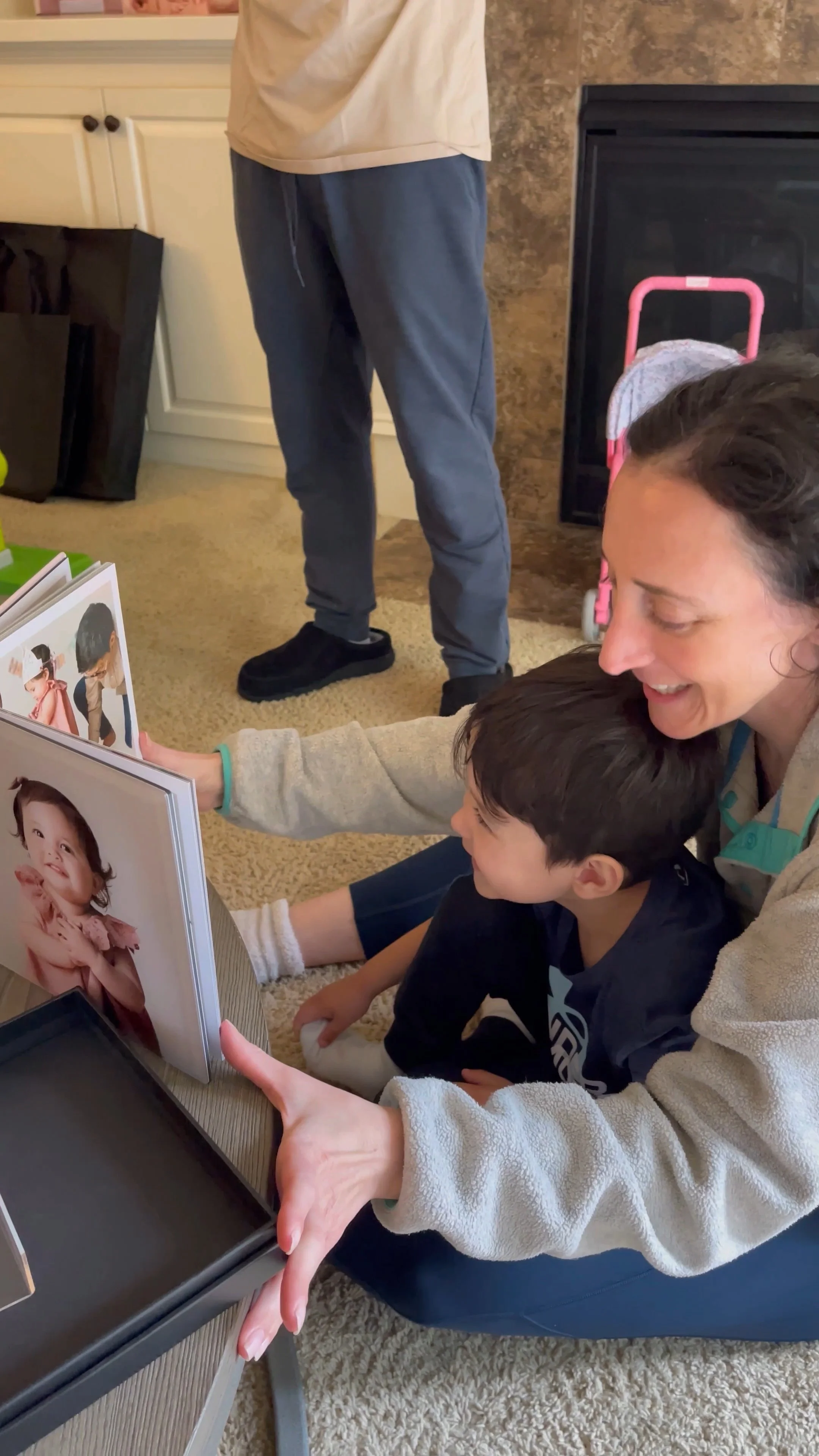 This image documents the "reveal" stage of a full-service portrait experience, highlighting the emotional impact of tangible heirloom products. The photograph shows a mother and her son gathered in their home to enjoy a custom-designed, museum-qualit