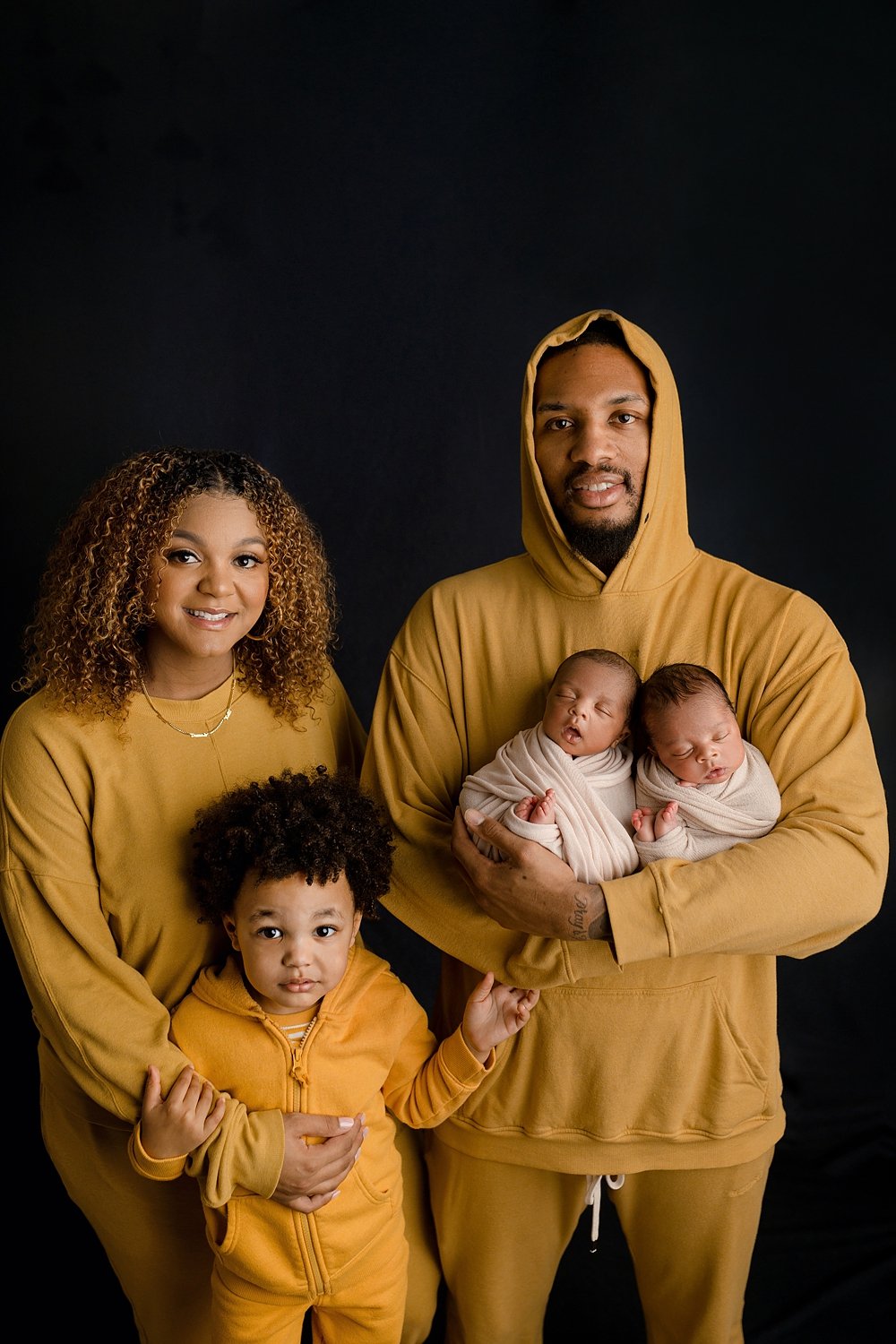 A professional studio portrait by Sunnymelon Photography featuring Damian Lillard and his family of 5, including his wife and children wearing matching mustard yellow outfits while holding newborn twins.