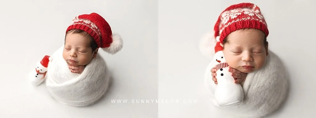 Sleeping newborn baby in a white knit wrap and red festive hat posing with a tiny snowman prop.