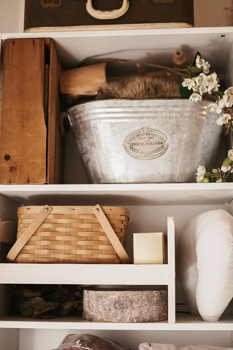 Shelving unit filled with professional newborn photography props like wooden crates, antique basins, and posing pillows for baby photo sessions in Portland, OR.