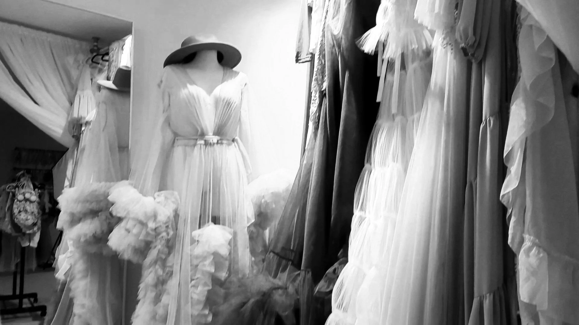 Black and white photo of the Sunnymelon Photography client closet, showcasing a rack of luxurious, flowing maternity gowns and dresses available for use during maternity photo sessions.
