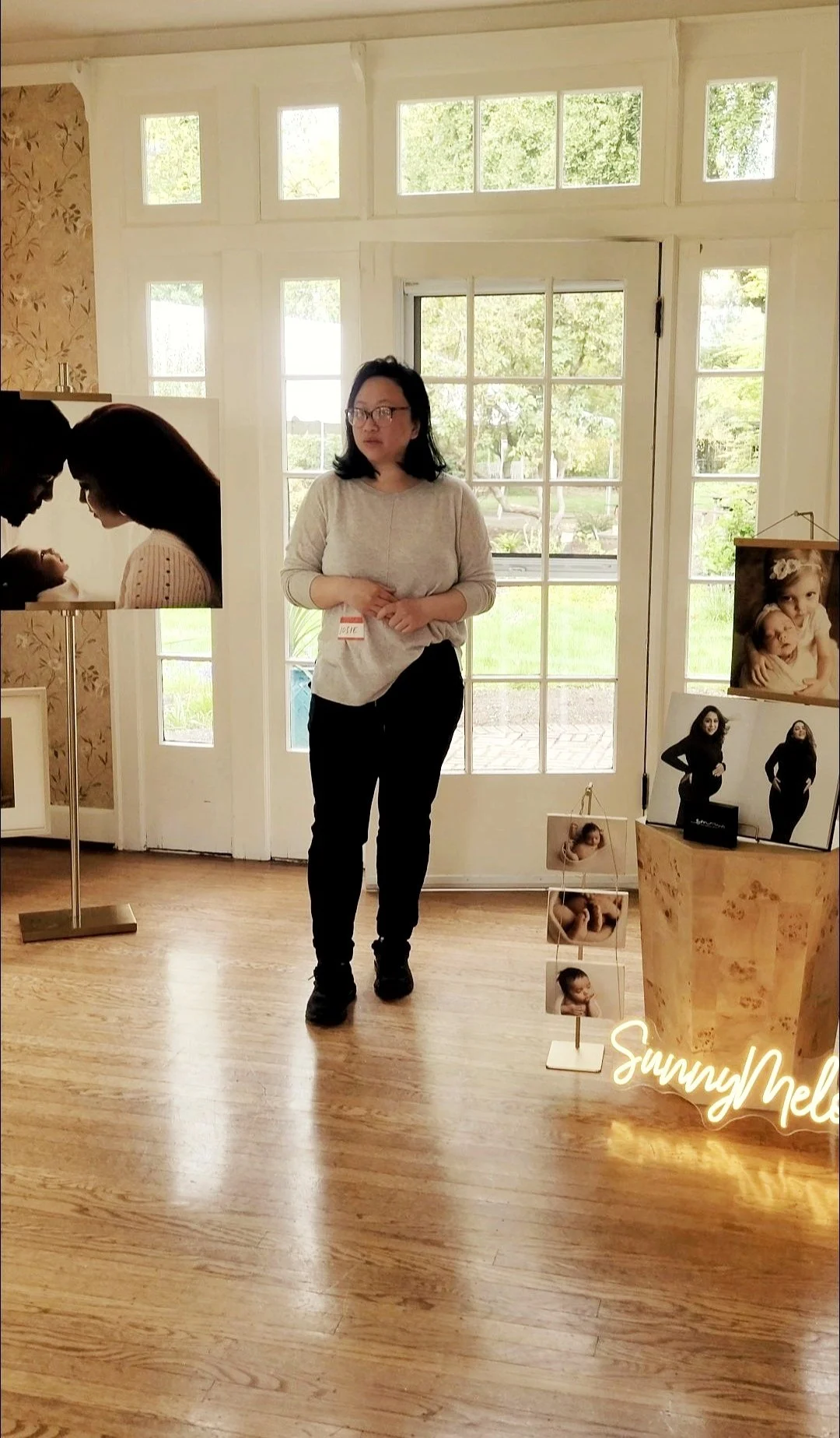 Professional photographer, Josie Tan, with an exhibit featuring large print portraits, maternity albums, and a custom neon sign in a bright studio space.