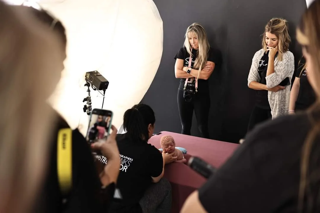 Behind-the-scenes of a newborn photography workshop featuring an instructor posing a baby under professional studio lighting.