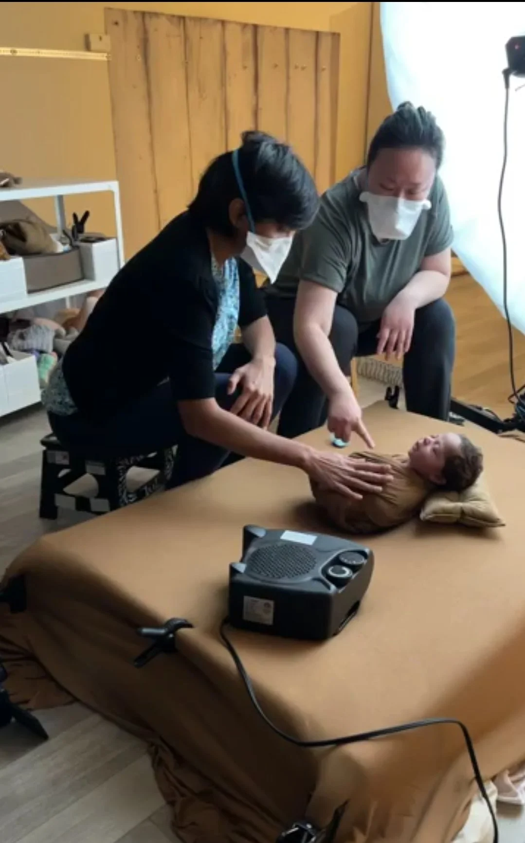 Professional photographers wearing masks while carefully posing a newborn during a studio training session.