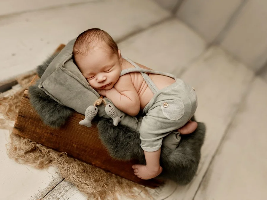 A sleeping newborn baby lying on a small wooden platform, wrapped in a gray hoodie and sweatpants with a soft furry blanket underneath.