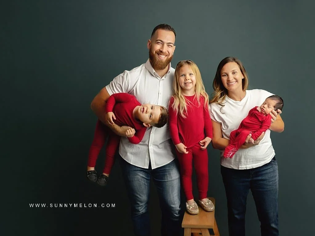 Happy family of five posing for a holiday portrait with a father playfully holding his son upside down.