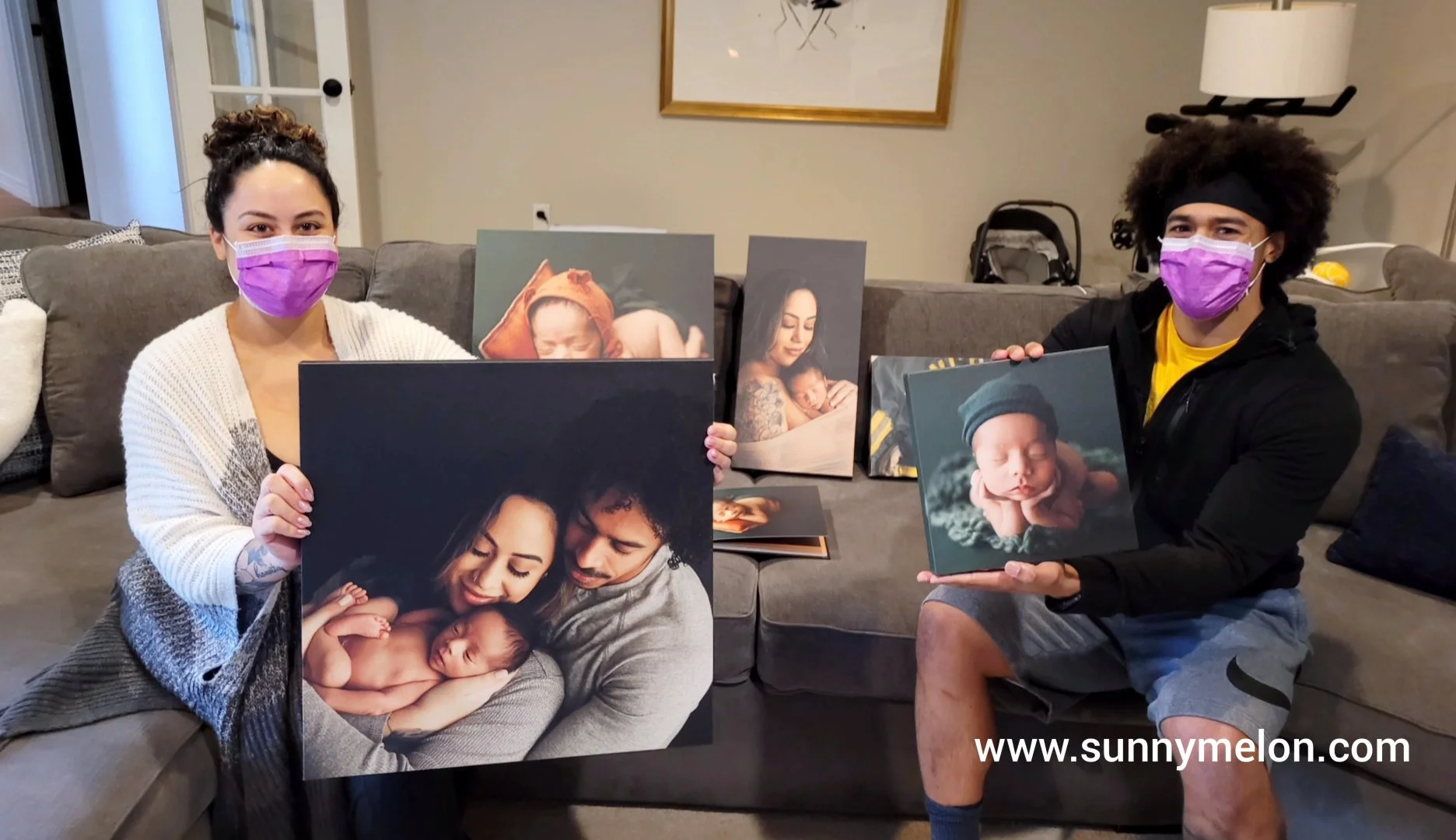 This heartwarming photo shows a couple proudly displaying a collection of high-quality canvas wraps from their professional photography session. They are holding a large family portrait and several smaller newborn canvases, illustrating the transitio