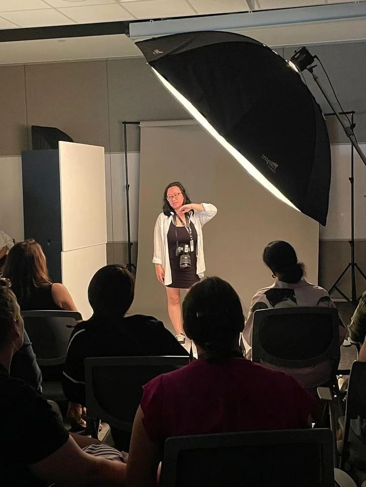 Josie Tan leading a photography education workshop, standing in front of a studio setup and speaking to an audience of students.