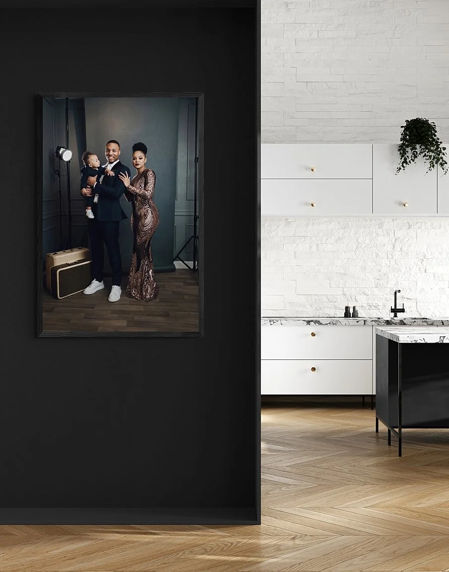A large, vertical professional family portrait of Damian Lillard, Kay'La and Dame Jr in formal attire, custom-framed and mounted on a matte black accent wall in a minimalist modern kitchen with herringbone wood floors.