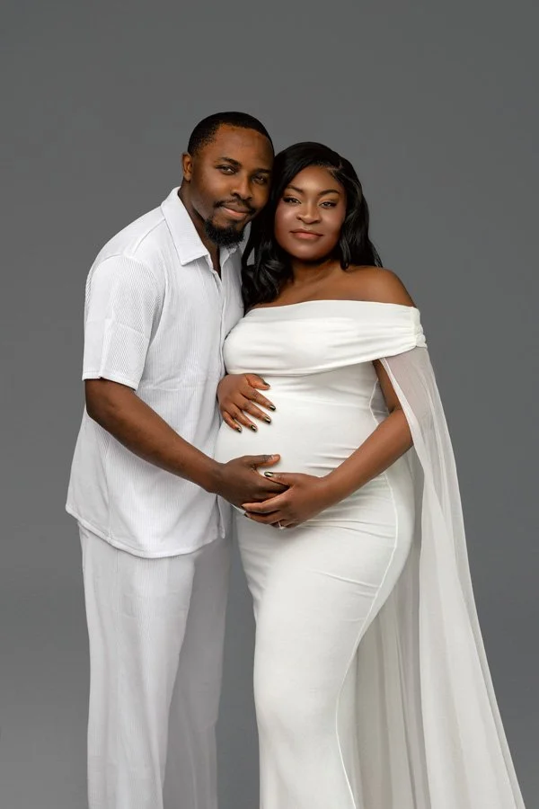 Beautiful Oregon couples maternity photo of a pregnant woman in a white dress and her partner, posed in a studio against a neutral gray background.