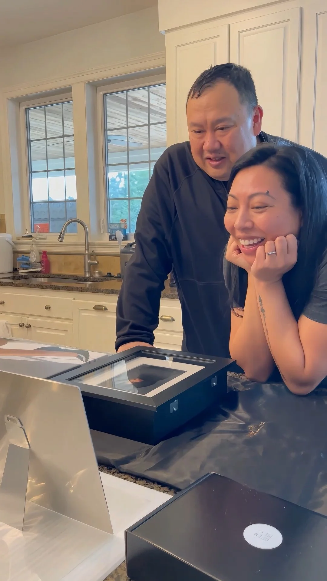 This photograph documents the crucial client reveal moment, the culmination of a high-end portrait session in Portland, Oregon. An expectant couple is captured unboxing their custom, museum-quality heirloom framed portrait, their faces radiating genu