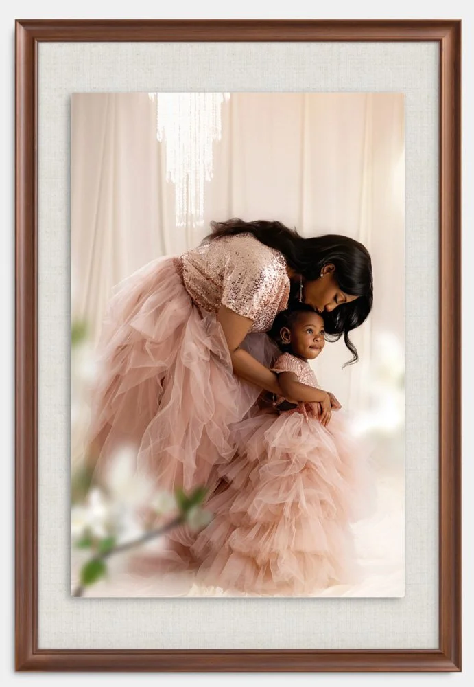 A woman and a young girl wearing matching pink, ruffled dresses, with the woman bending over and holding the girl, in a softly lit indoor setting.