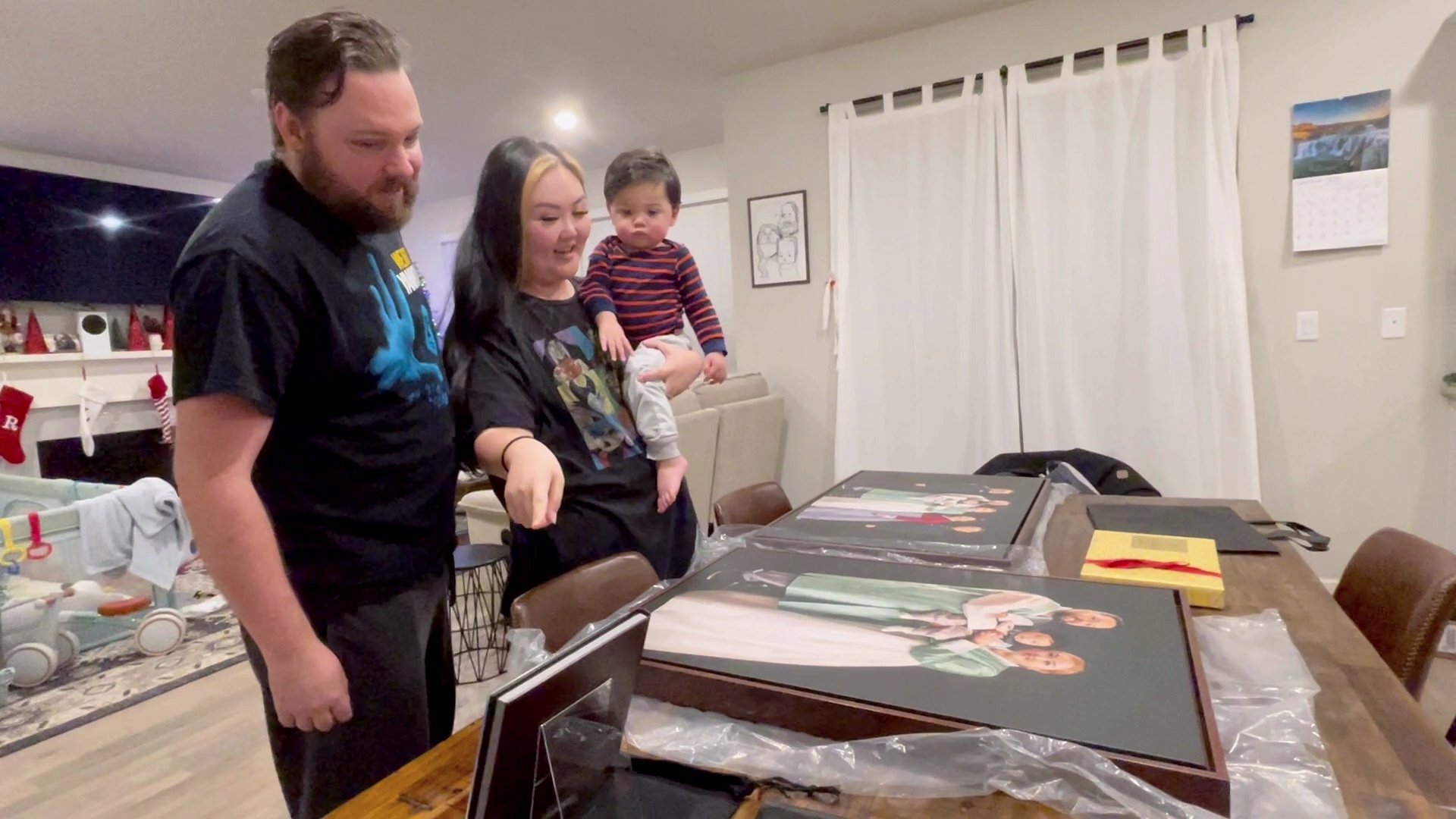 A woman carefully examines a black framed photo on a table surrounded by several large family portrait canvases.