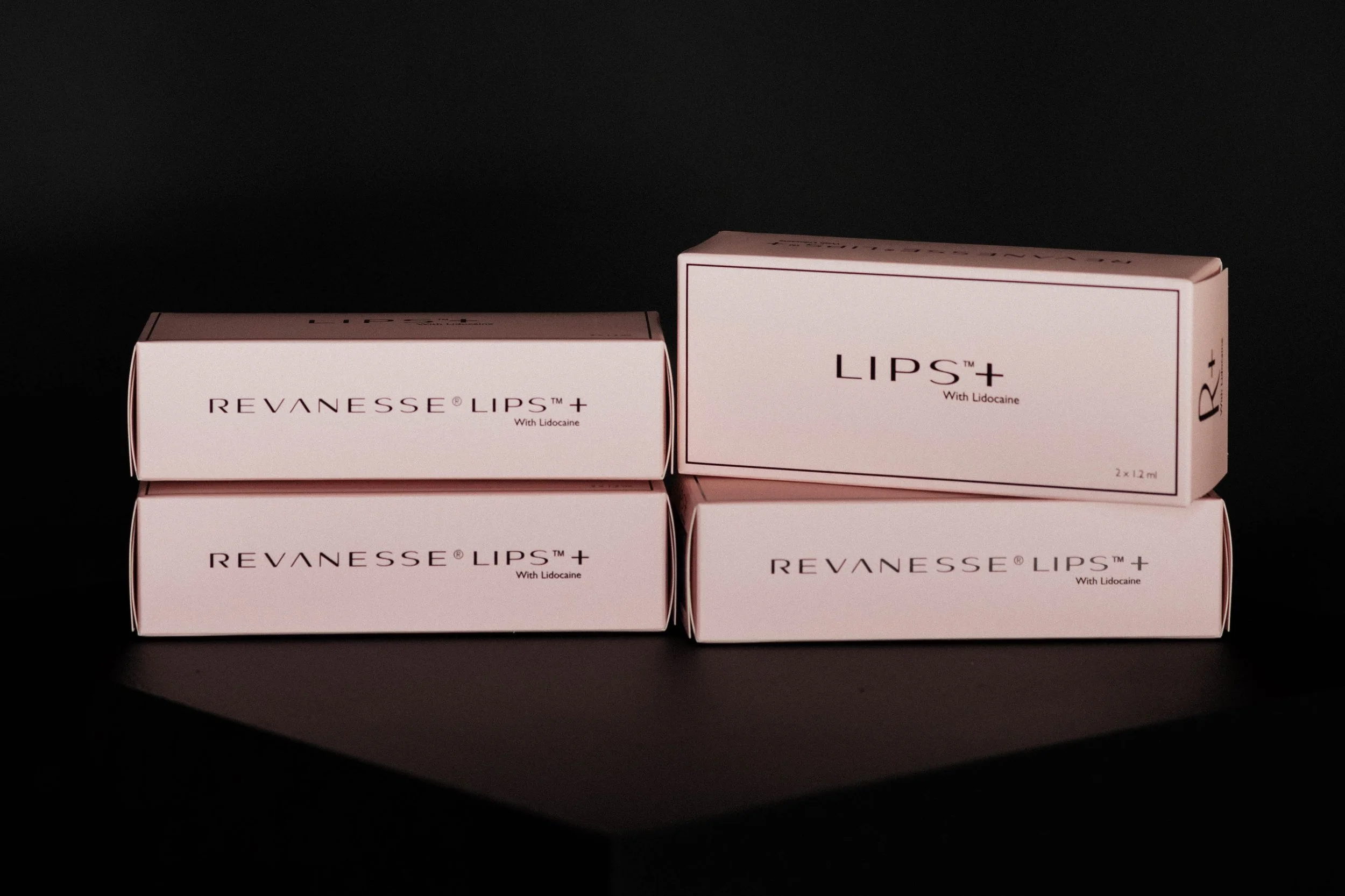 Four boxes of REVANESSE LIPS+ with Lidocaine, pink packaging, arranged against a black background.