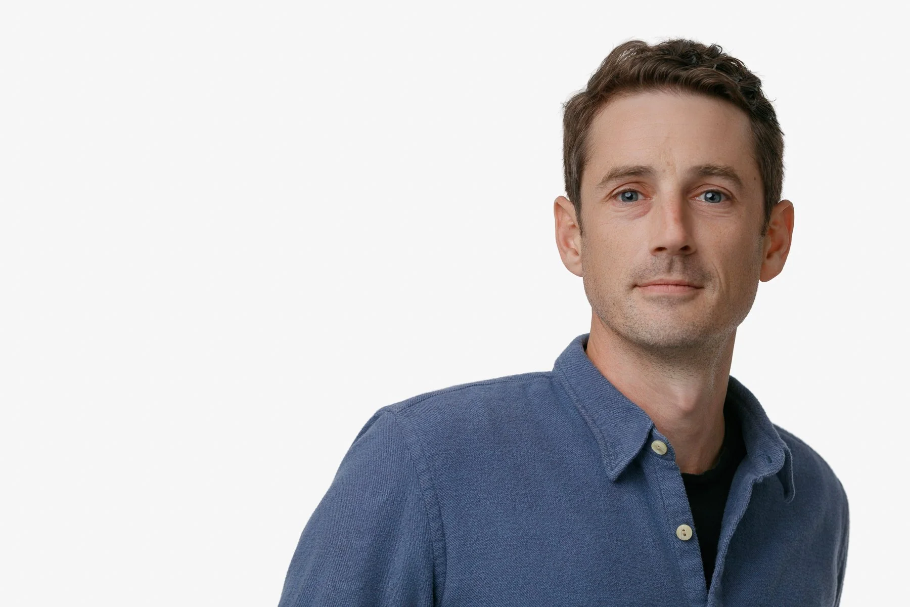 A person dressed in a gray suit with a pink tie and a boutonniere, standing in front of an archway.